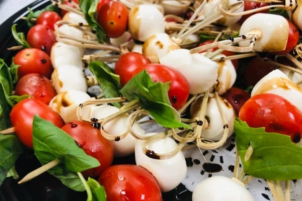 Skewers of tomatoes, mozzarella balls, and basil on a plate.