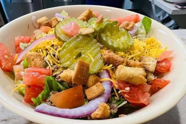 A salad bowl with croutons, tomatoes, cheese, pickles and red onions.