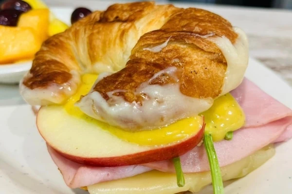 A croissant sandwich with ham and apples on a plate.