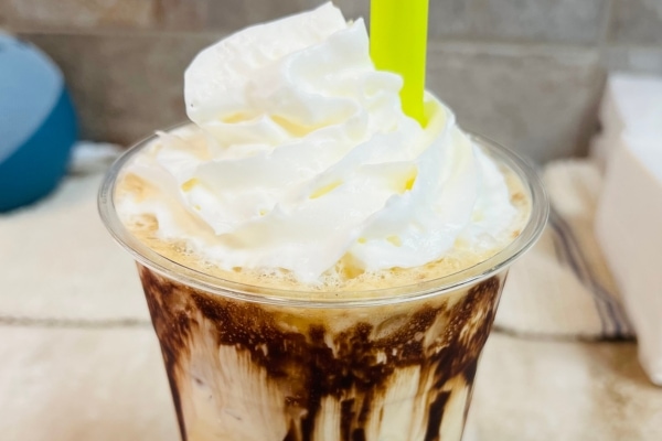 An iced coffee topped with whipped cream and served with a green straw.