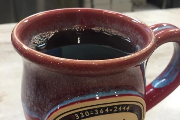 A red mug with black coffee in it sits on a counter.