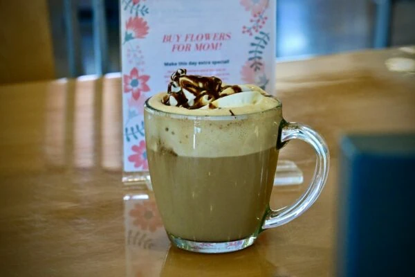 A mocha with whipped cream and chocolate on a table.