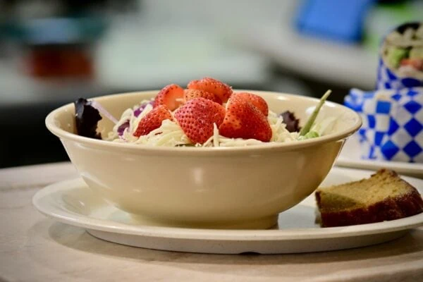 A bowl of salad with strawberries, cheese, and onions and a piece of bread on the side.